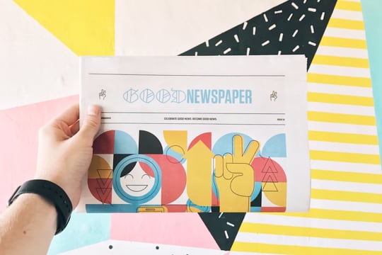 hand holding a newspaper in the background of yellow, pink and black